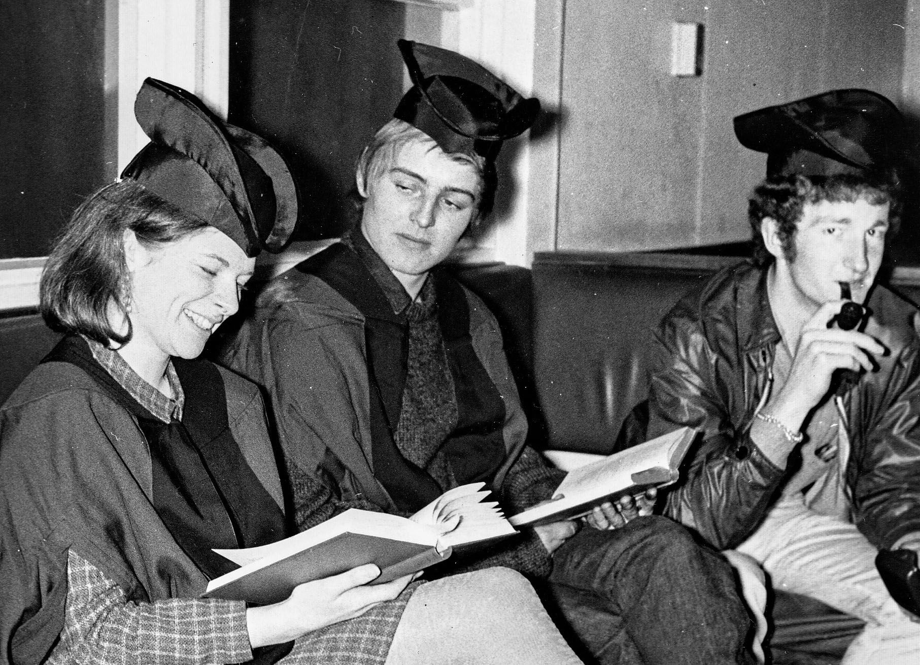 A black and white image of three students in full gown studying at the LCR.