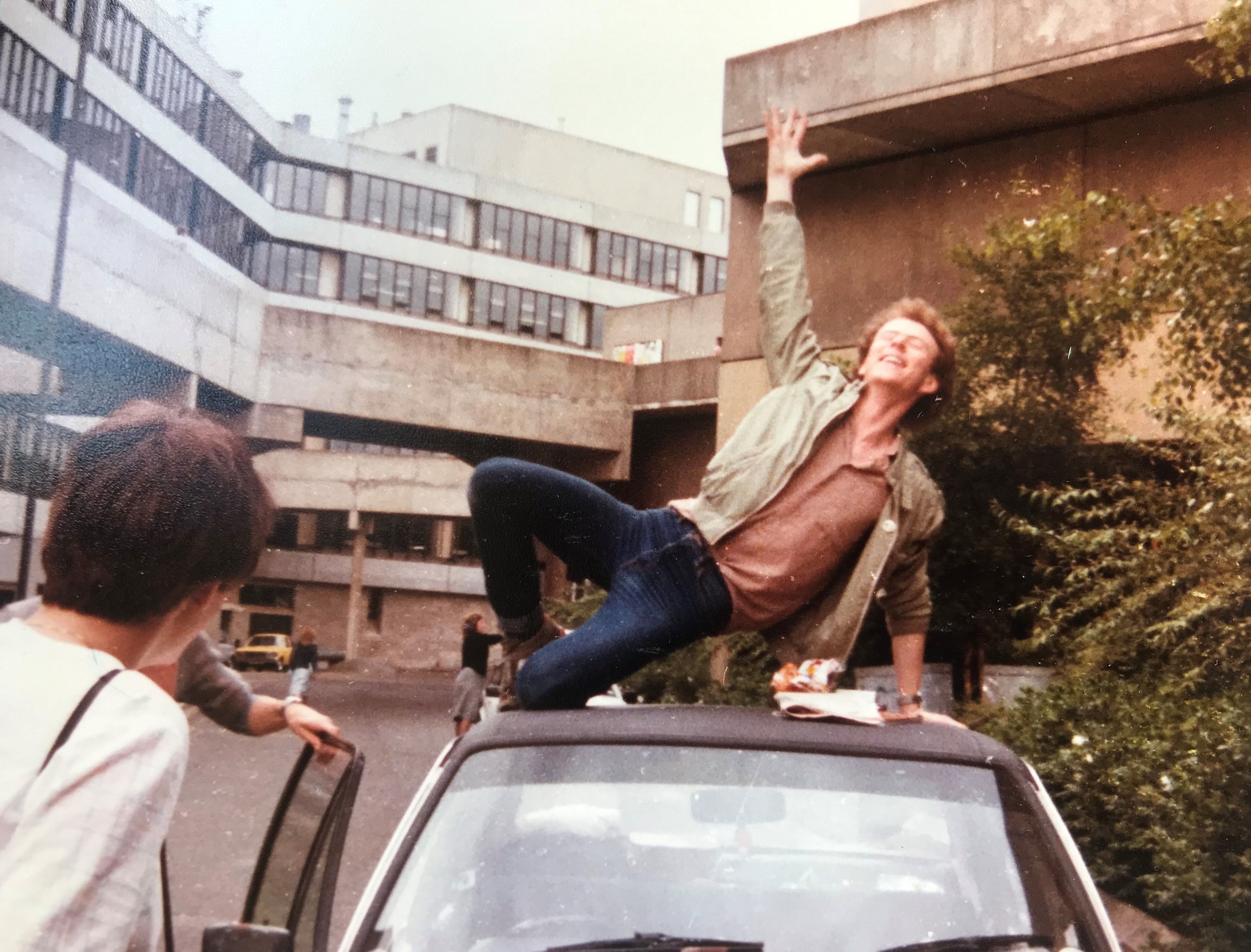 A picture of Andrew on top his MkII Ford Escart outside his room in Norfolk Terrace. His right arm is raised above him and he carries a broad smile.