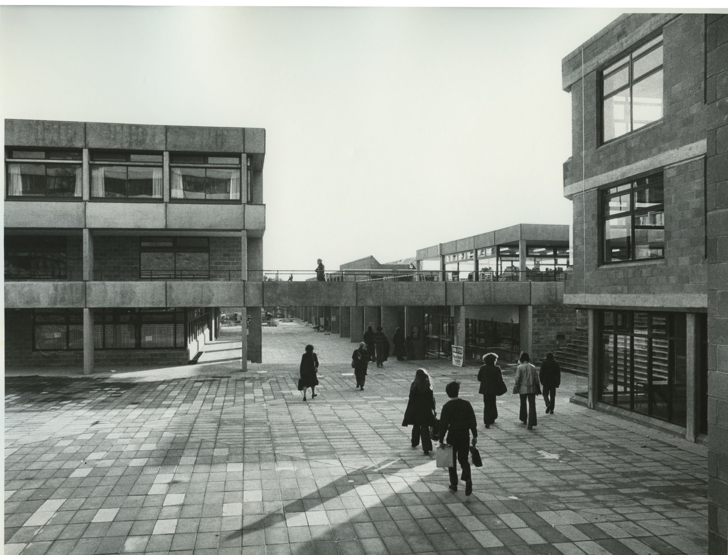 Archival black and white image of the Square from the 1970s. Students walking towards the street. Brutalist architecture.