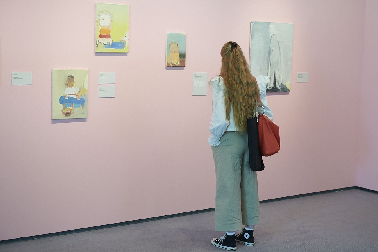 person looking at paintings on the wall of art gallery