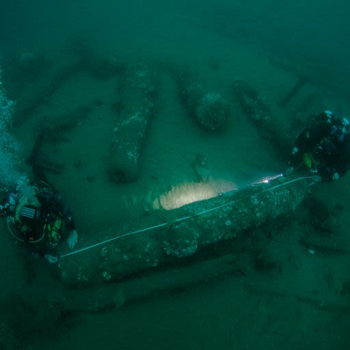 Two divers hold a tape measure against a barnacle-covered canon