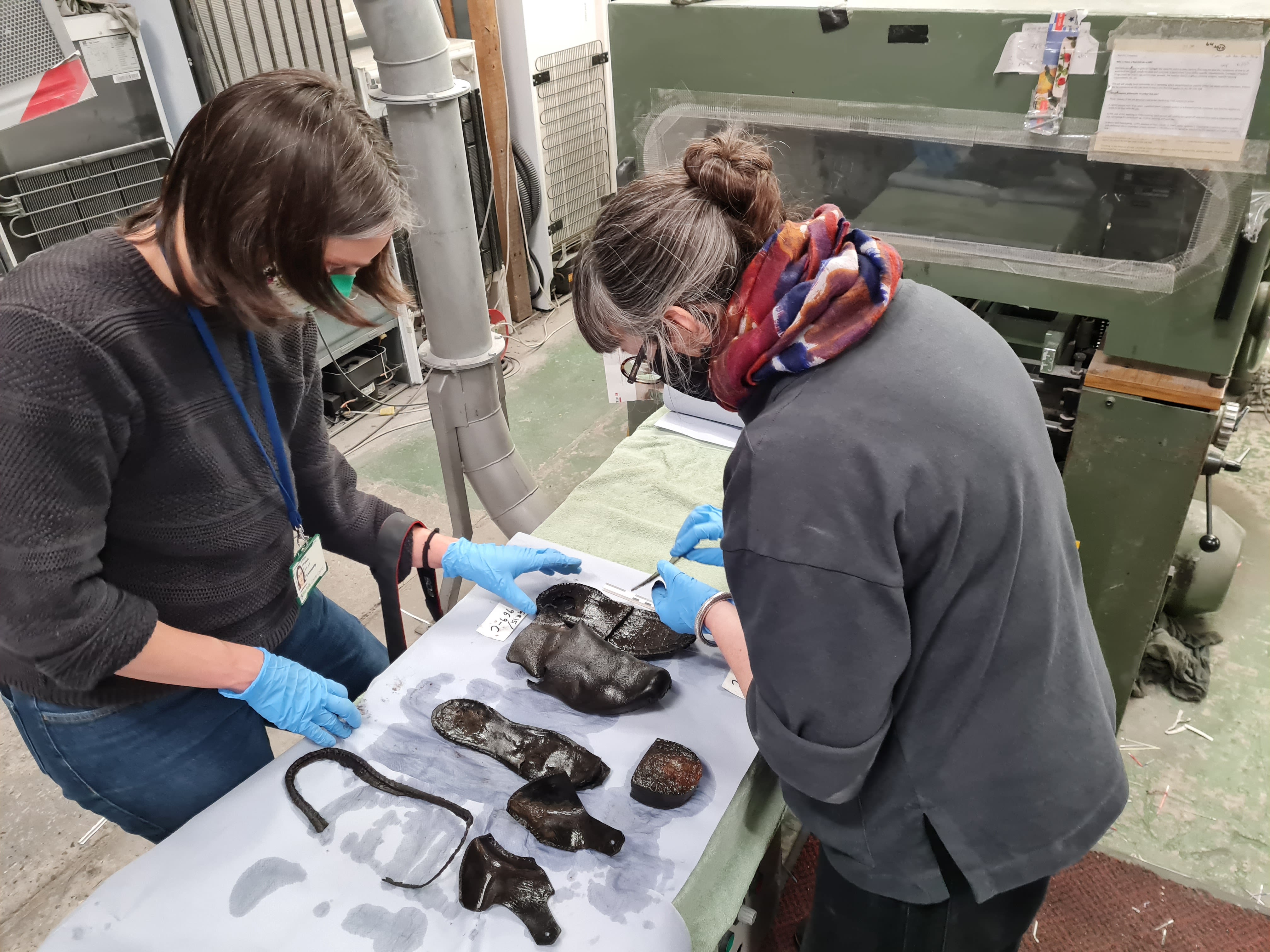 Two women in masks and gloves carefully handle artefacts