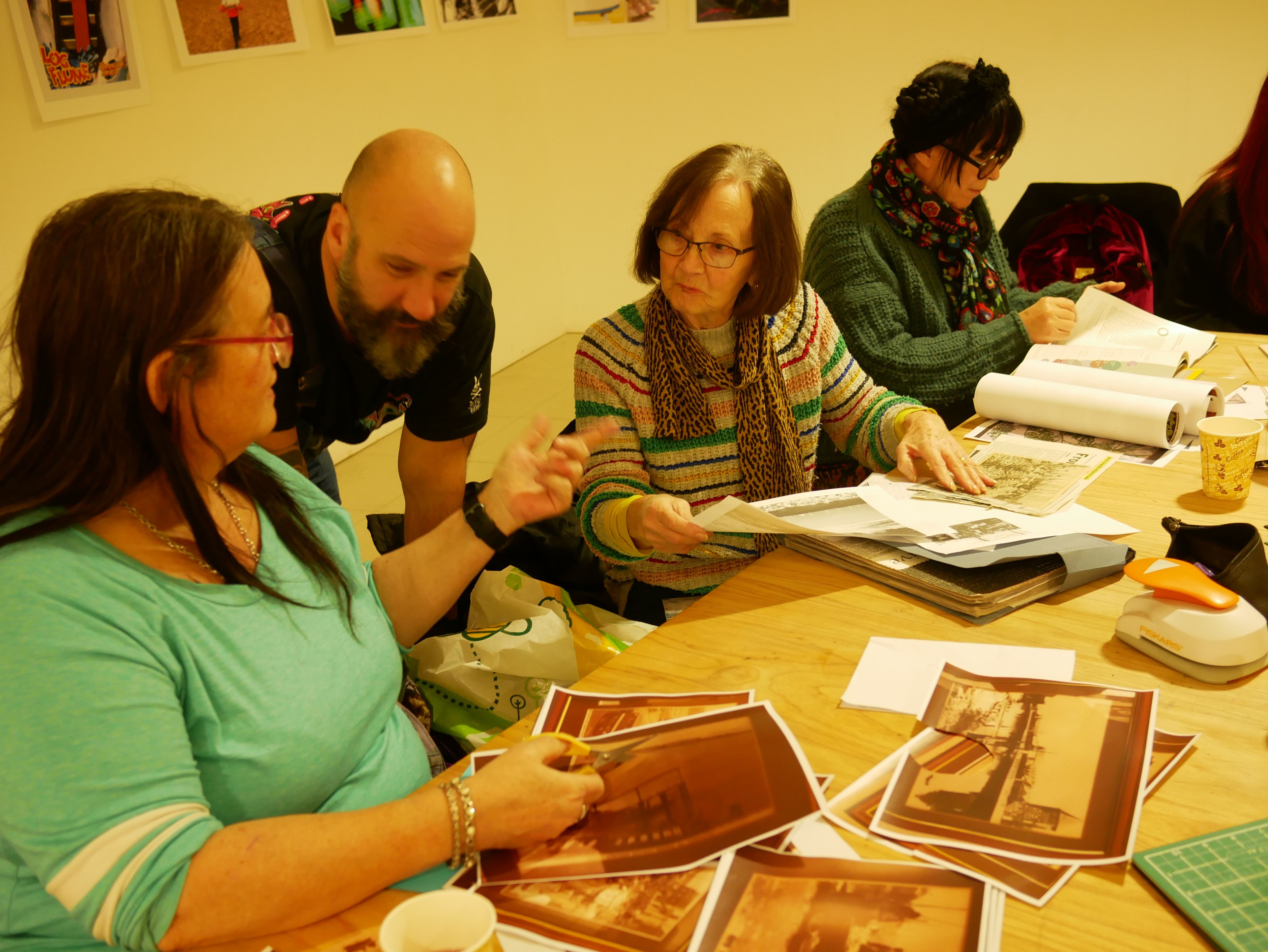 Two seated women and a standing man have a conversation besides a table that contains old photographs of Great Yarmouth.