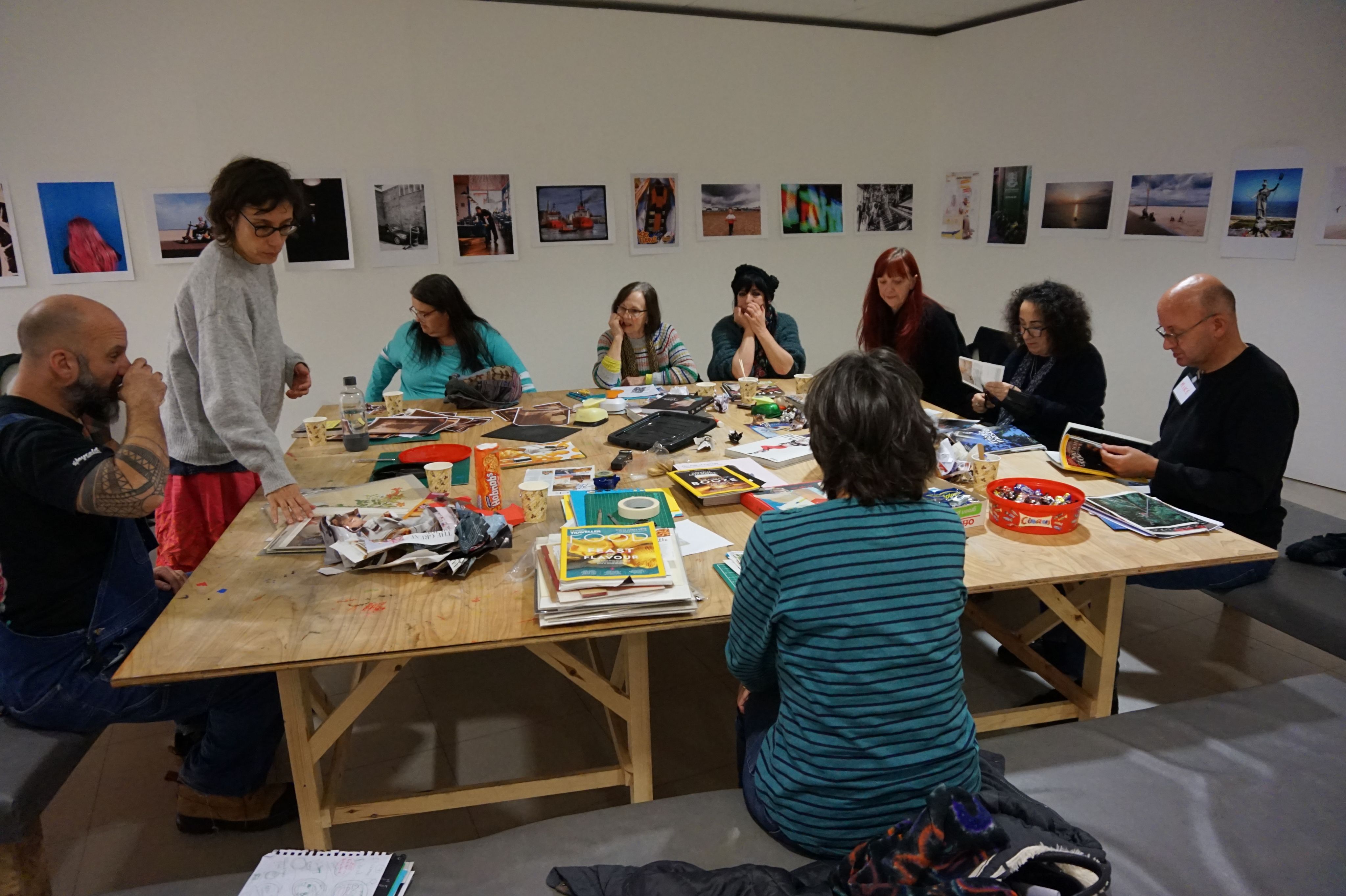 Eight people sit round a table, participating in a collage workshop at PrimeYarc Gallery, led by Maria Abranches and Elena Horton from UEA's School of International Development