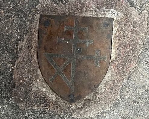 A merchants' mark carved into metal and embossed onto a stone floor.