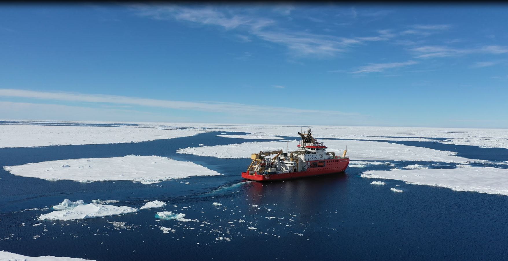 A ship sails through a sea covered in ice floe.