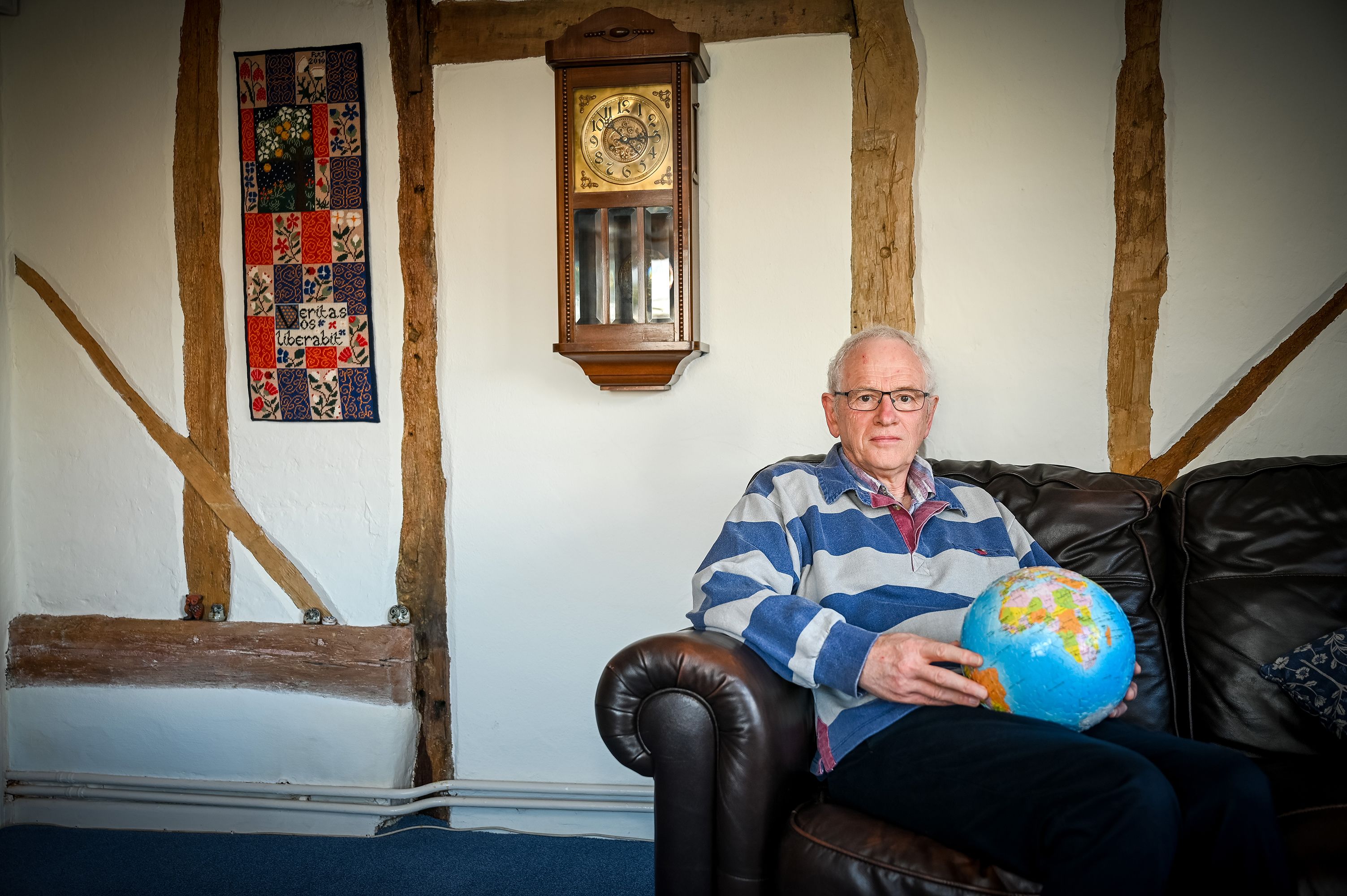 man holding a globe sat on a leather sofa in a timber framed house