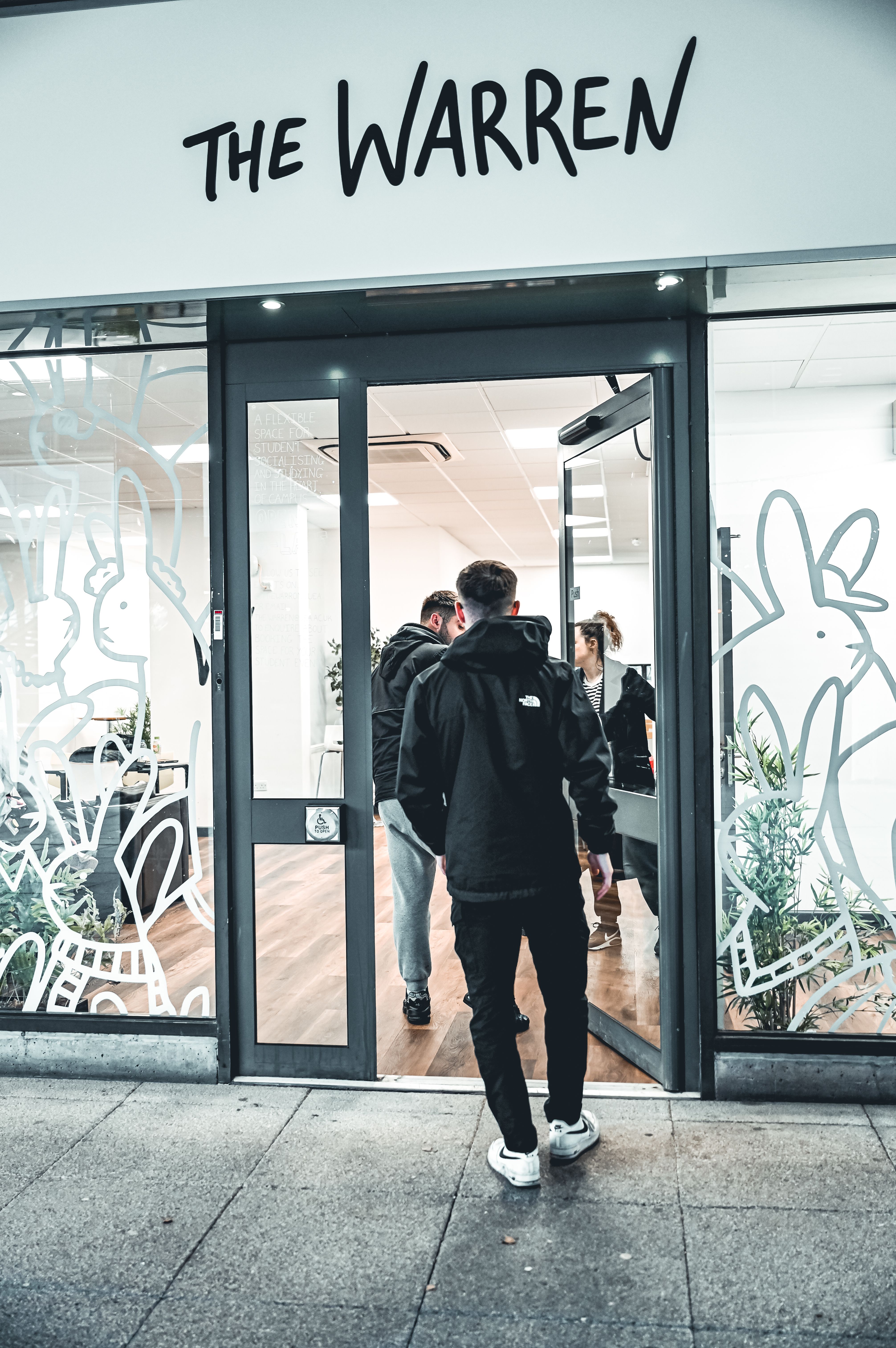Three people entering a door to The Warren, with white line artwork of bunnies on the windows