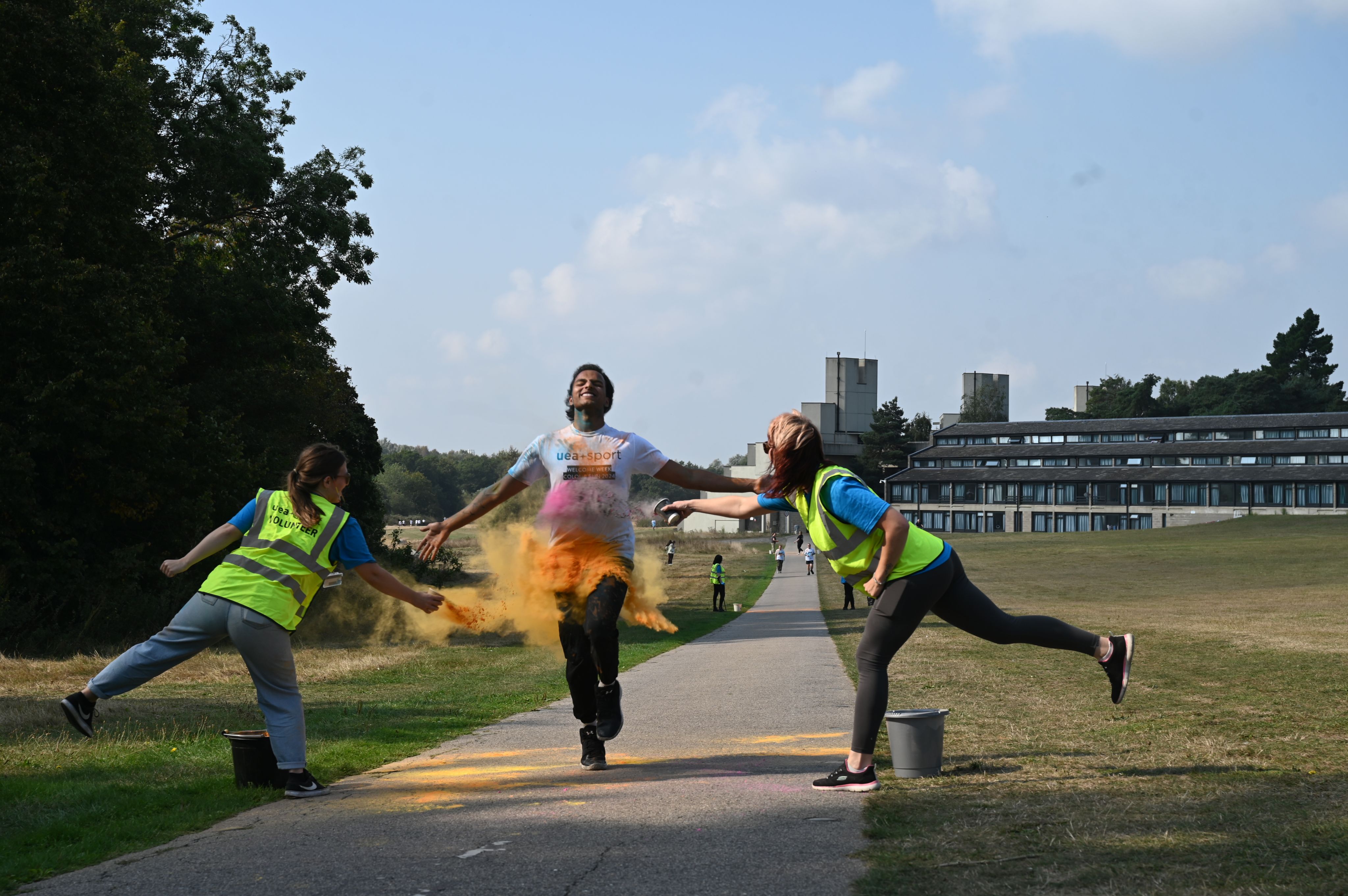 Two people in high vis jackets throwing orange powder over a student on the Colour Run