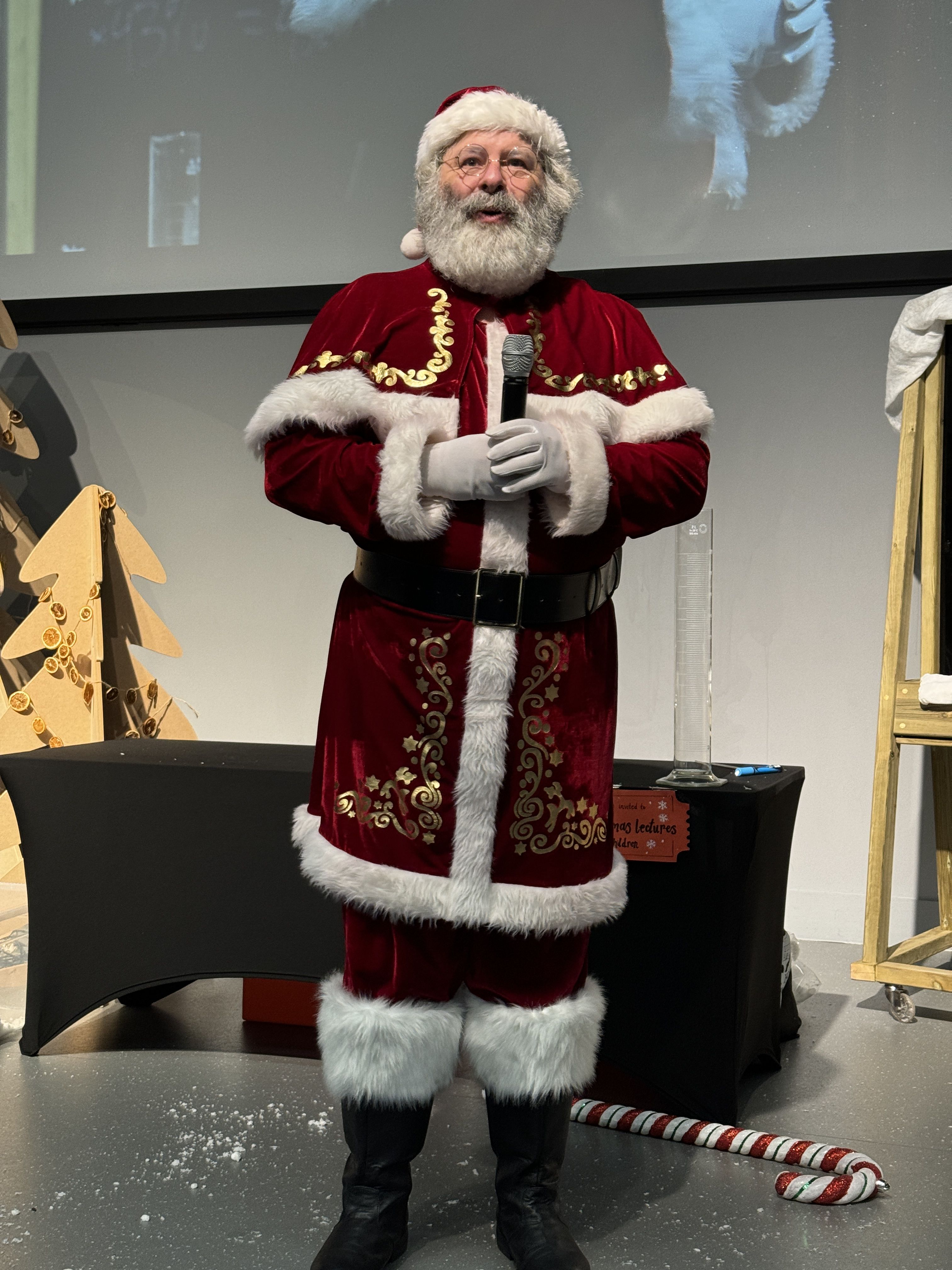 Santa Claus dressed in his red and white Santa suit and hat on stage in a lecture theatre