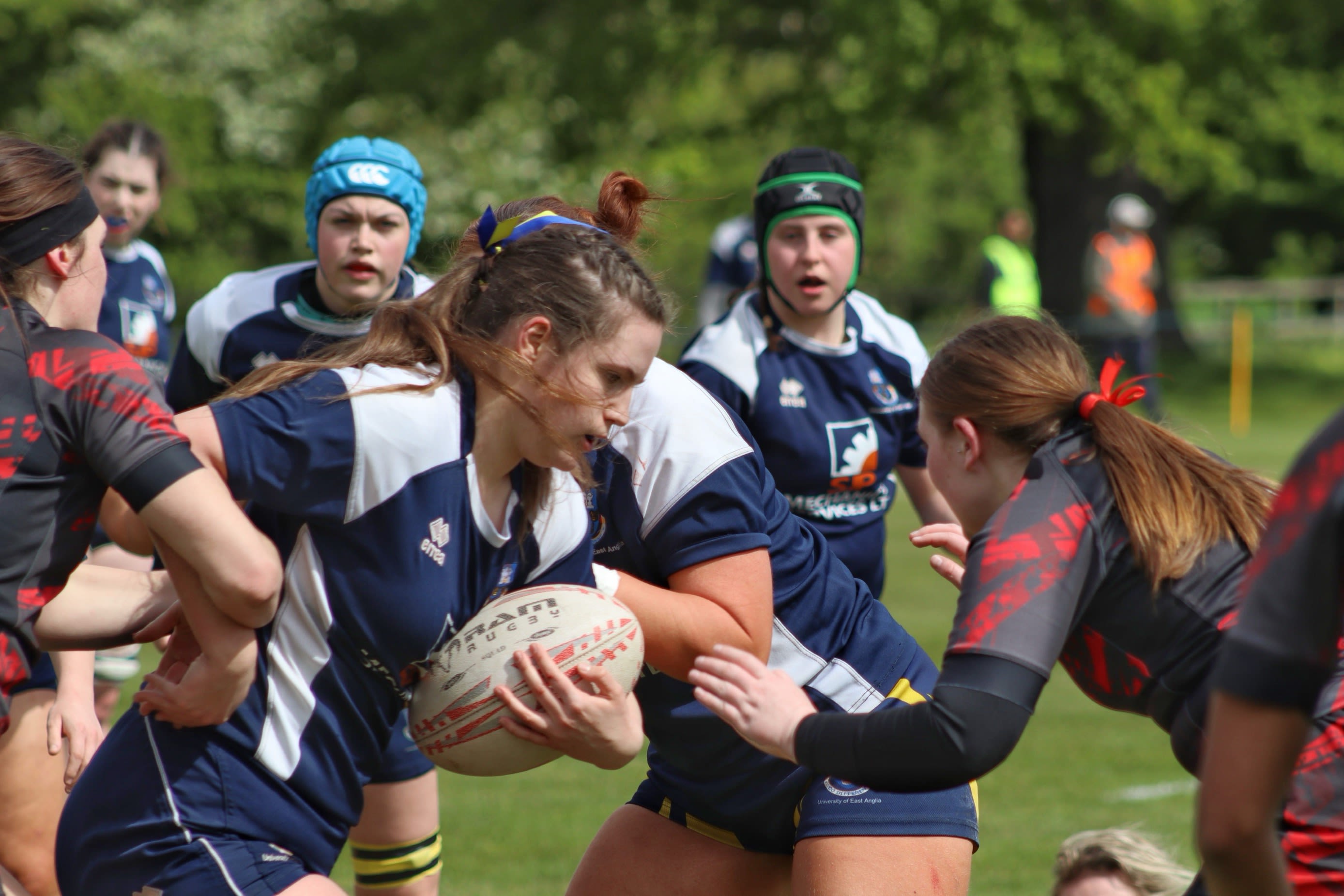 Rugby club members of UEA and Essex huddled together, a rugby ball in one of their hands