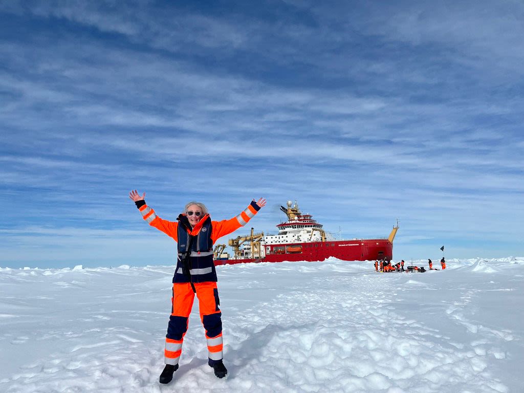 A woman in an orange jumpsuit on the ice in front of a red boat