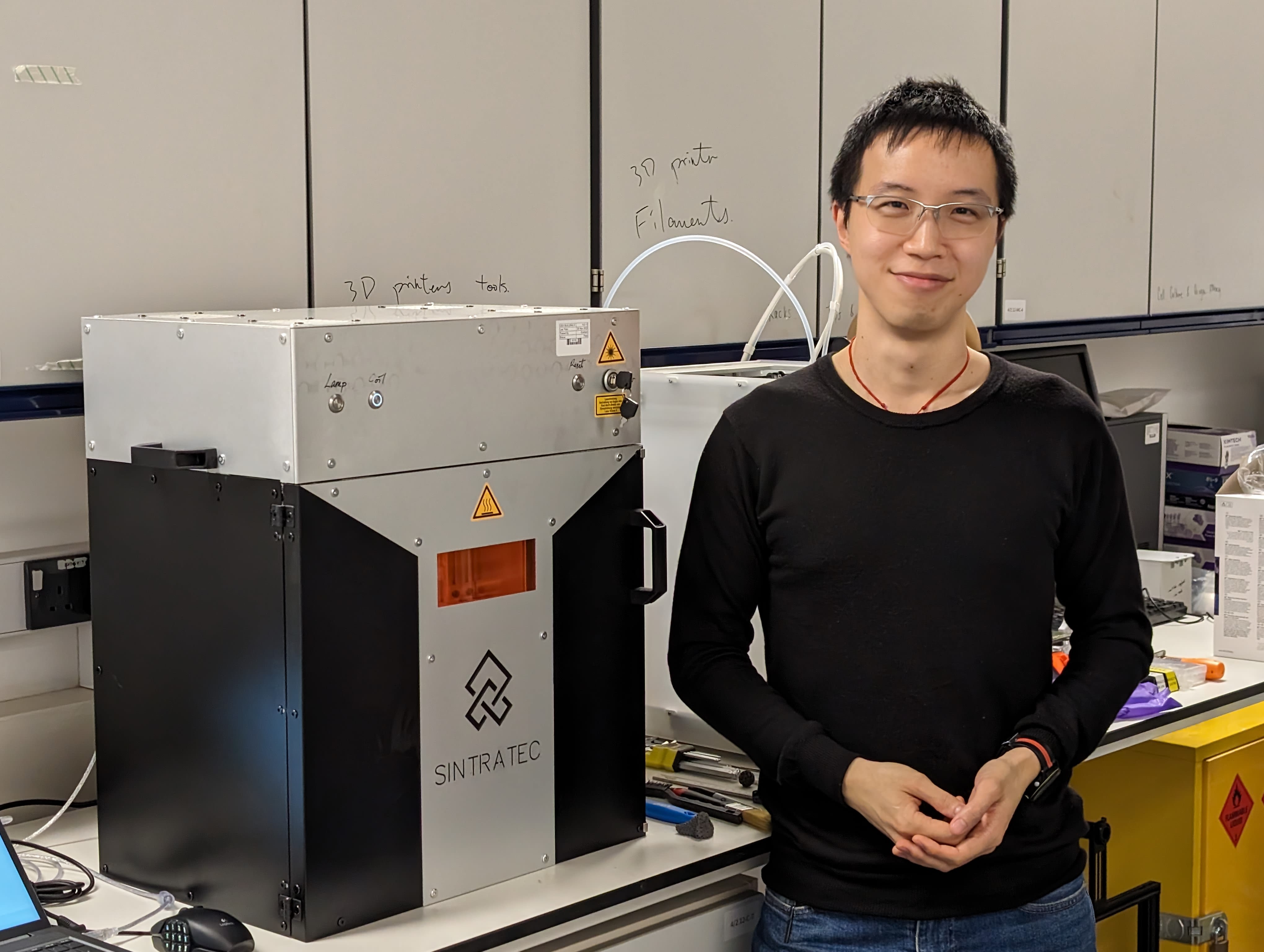Ken Tam standing next a 3D printer in a laboratory