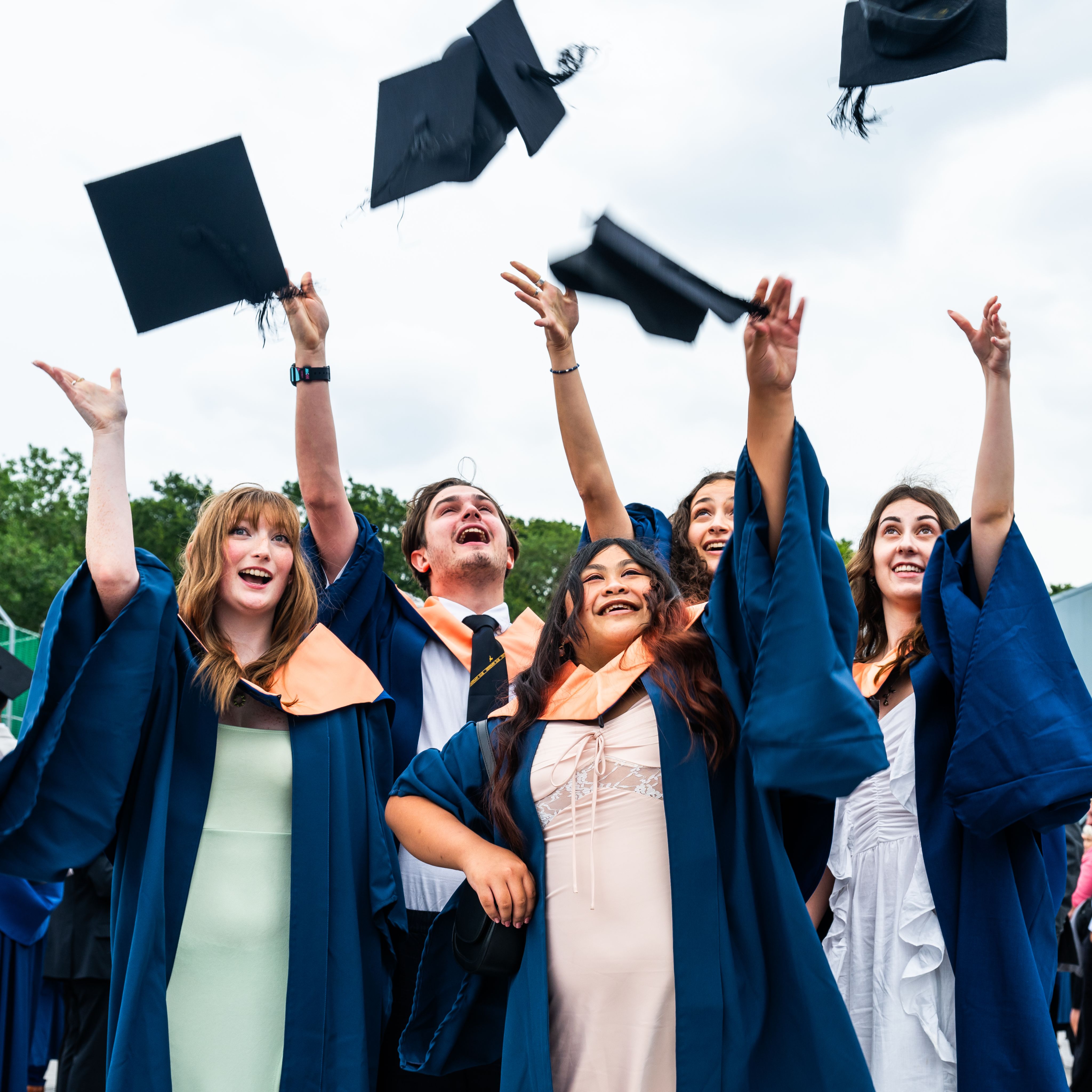 Students smiling and throwing mortarboards in the air at a graduation ceremony
