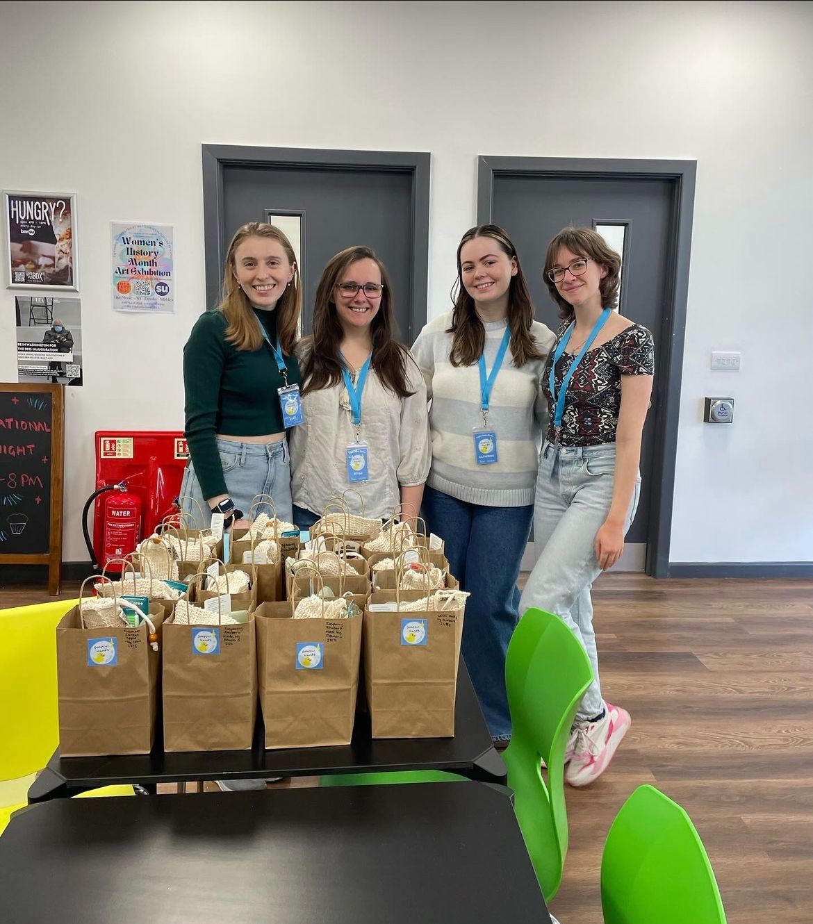 Four members of Soapful Hands smiling behind a table of brown bags, which are full of completed hygiene kits