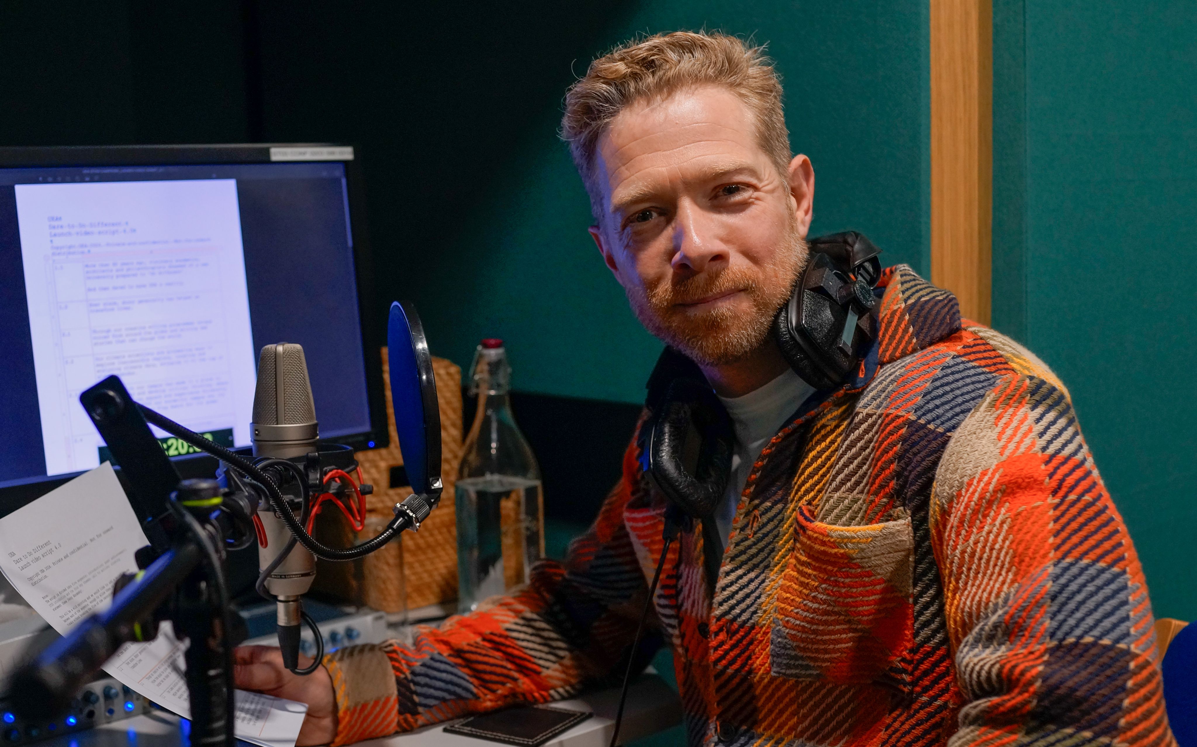 Zeb Soanes in a red checked jacket next to audio recording equipment