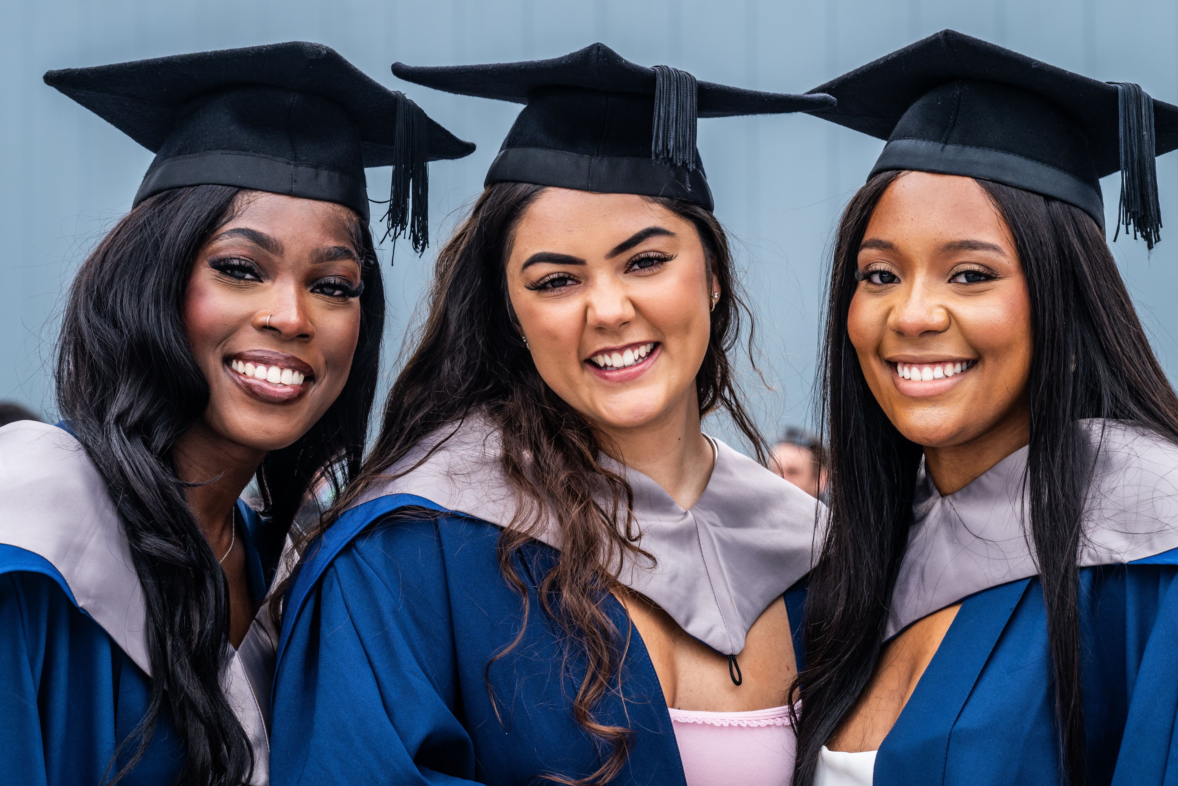 Three UEA graduates in blue robes and graduation caps