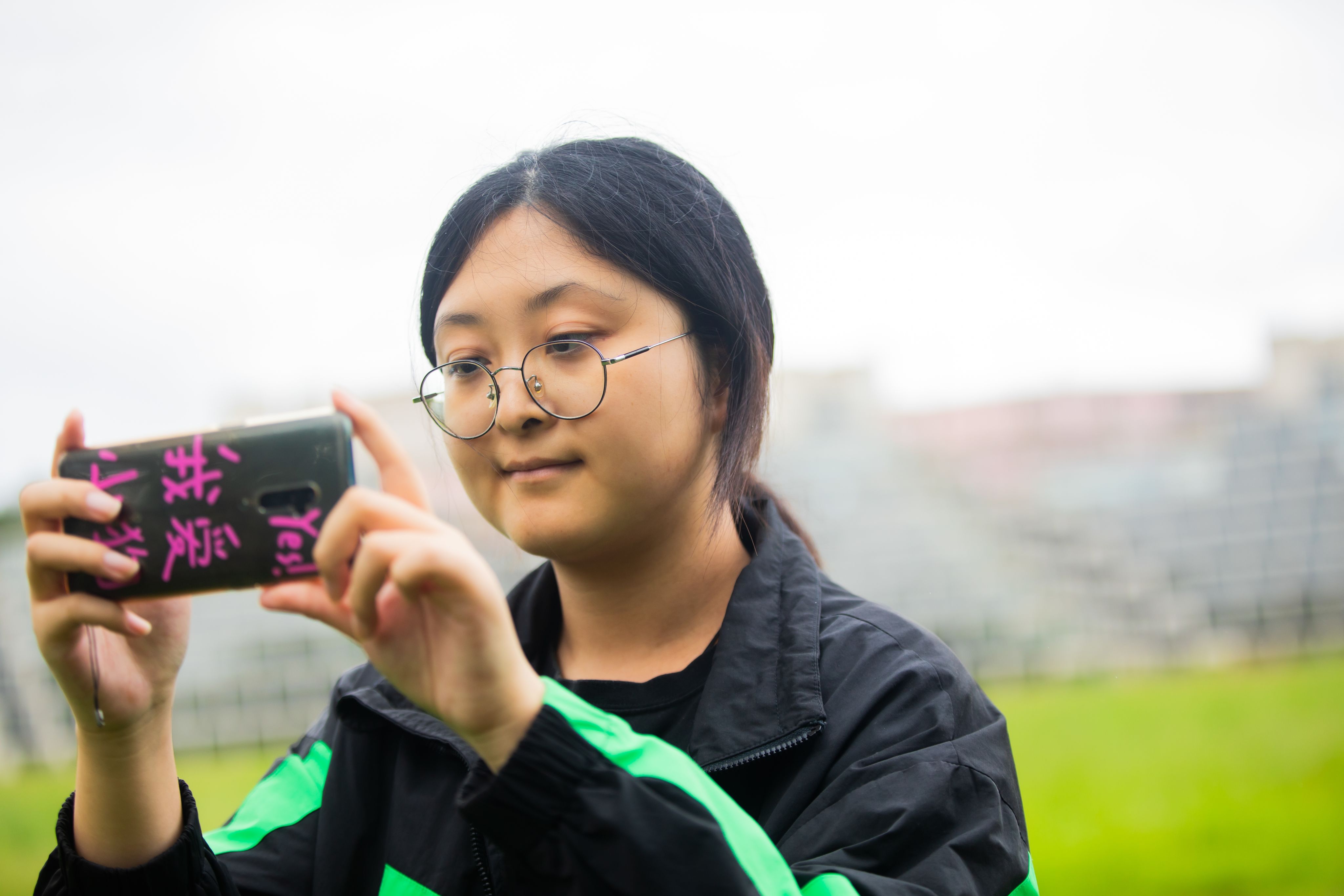 Huizhi Yang taking a picture with her phone on UEA's green campus